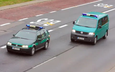 Dwa pojazdy uprzywilejowane Straży Granicznej, zielony kombi i turkusowy van, jadą drogą.