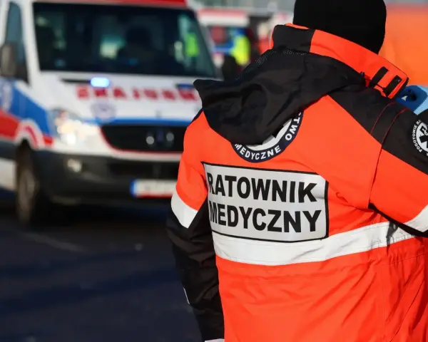 Ratownik medyczny w jaskrawej kurtce stoi obok karetki pogotowia.
