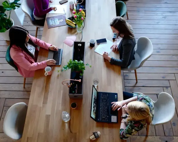 Kobiety pracują przy drewnianym stole. Jedna pisze na laptopie, druga notuje. To przykład, jak etyka co to, wpływa na codzienne zadania.