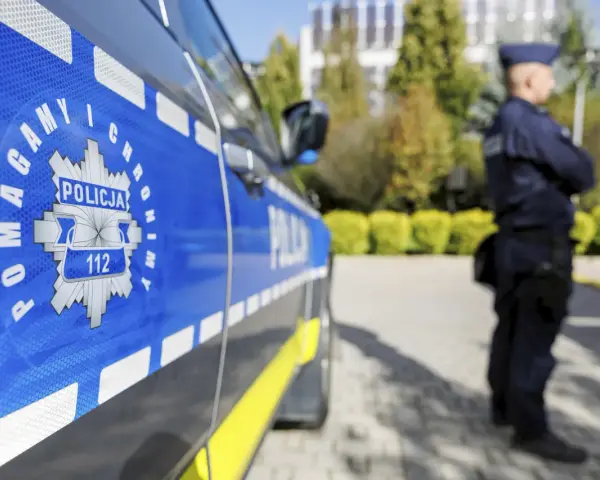Policjant w mundurze stoi obok radiowozu. Czy zarobki w policji są adekwatne do służby?