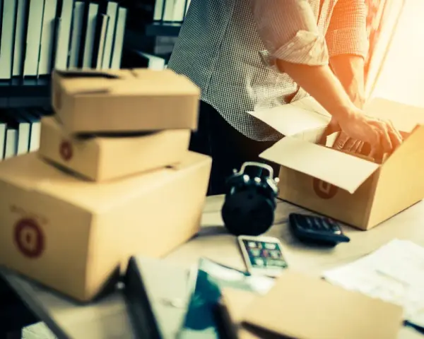Mężczyzna pakuje paczki, przygotowując się do ich wysyłki. Stosy pudeł i akcesoria biurowe sugerują pracę związaną z fulfillment.