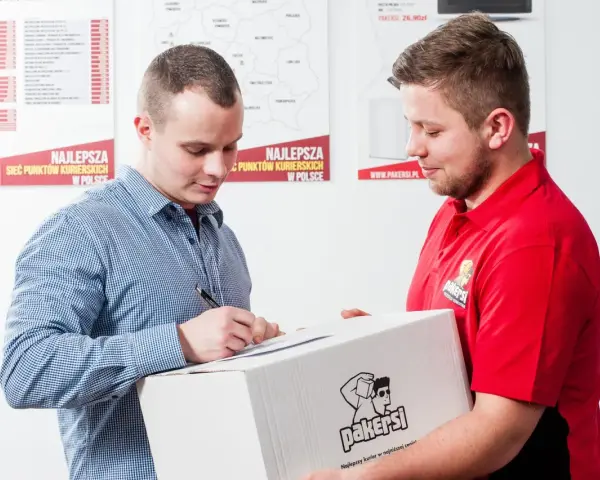 Kurier w czerwonej koszulce przekazuje paczkę, a klient podpisuje dokument. Zastanawiasz się, ile zarabia kurier?