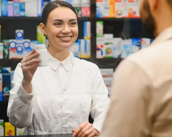 Uśmiechnięty farmaceuta podaje klientowi białe opakowanie leku.