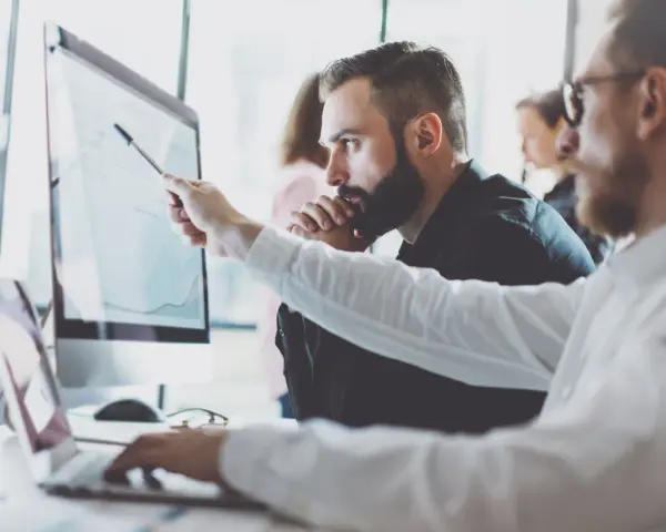 Analityk biznesowy wskazuje na wykres na monitorze, omawiając dane z kolegą.