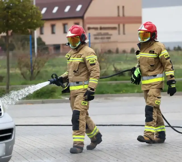 Dwóch strażaków PSP w akcji, jeden z wężem wodnym. Ciekawe, ile zarabia strażak w PSP za taką pracę.