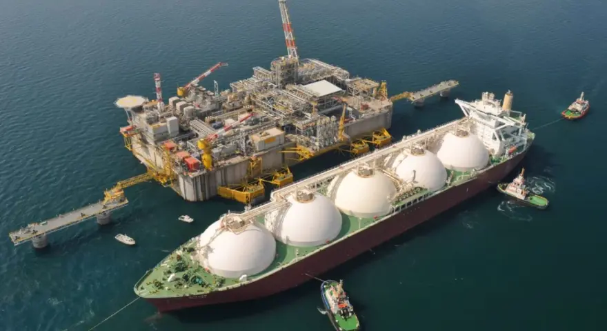 Statek LNG przycumowany do platformy wiertniczej na morzu, holowany przez holowniki.