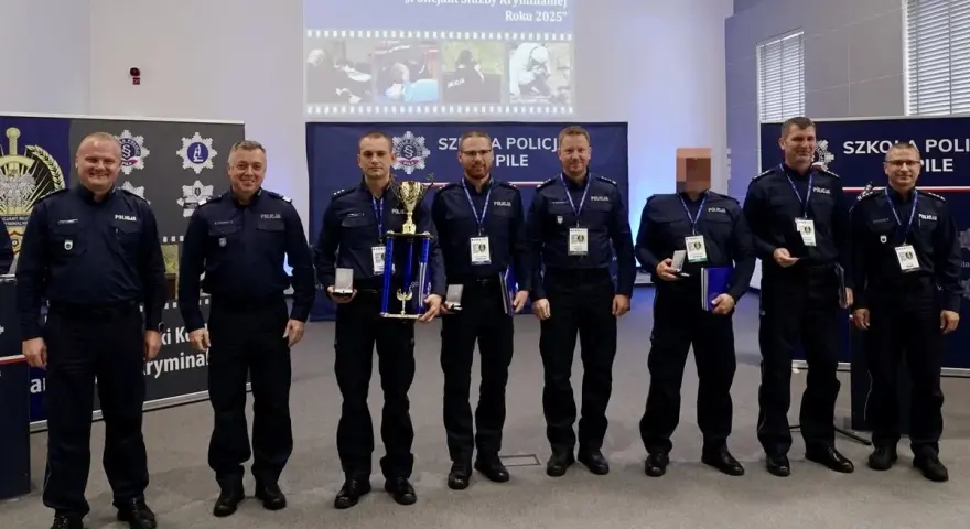 Policjanci w mundurach stoją w rzędzie, niektórzy trzymają nagrody i dyplomy.