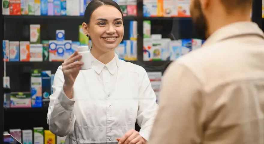 Uśmiechnięty farmaceuta podaje klientowi białe opakowanie leku.