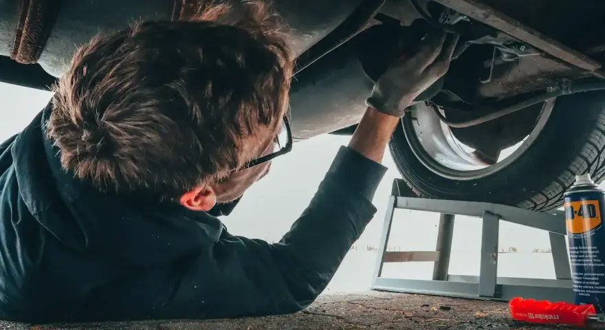 Mechanik w okularach naprawia podwozie samochodu, leżąc na ziemi.