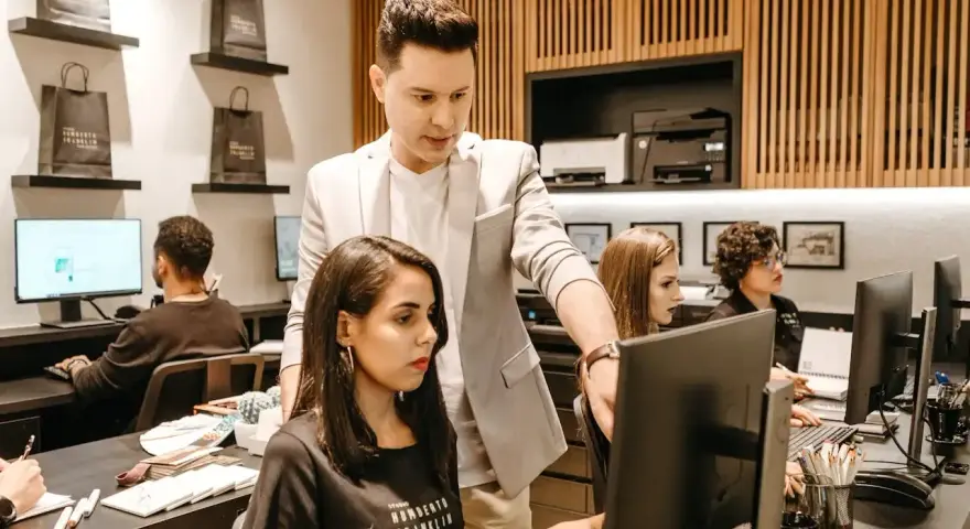 Koordynator w jasnej marynarce wskazuje coś na monitorze pracownicy.