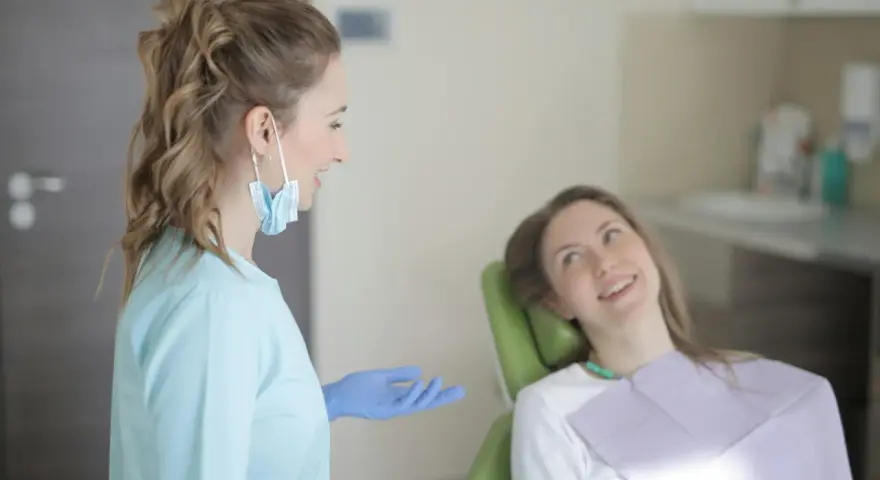 Uśmiechnięta pacjentka na fotelu stomatologicznym słucha dentystki. To obrazek z gabinetu, gdzie odbywają się studia stomatologiczne.