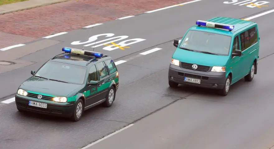 Dwa pojazdy uprzywilejowane Straży Granicznej, zielony kombi i turkusowy van, jadą drogą.