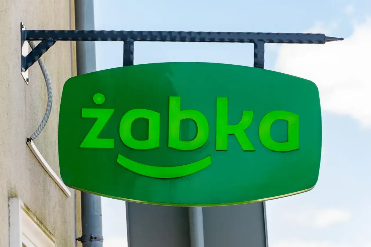Zielony szyld Żabki z uśmiechem. Zastanawiasz się, ile zarabia się w Żabce? Sprawdź oferty pracy!