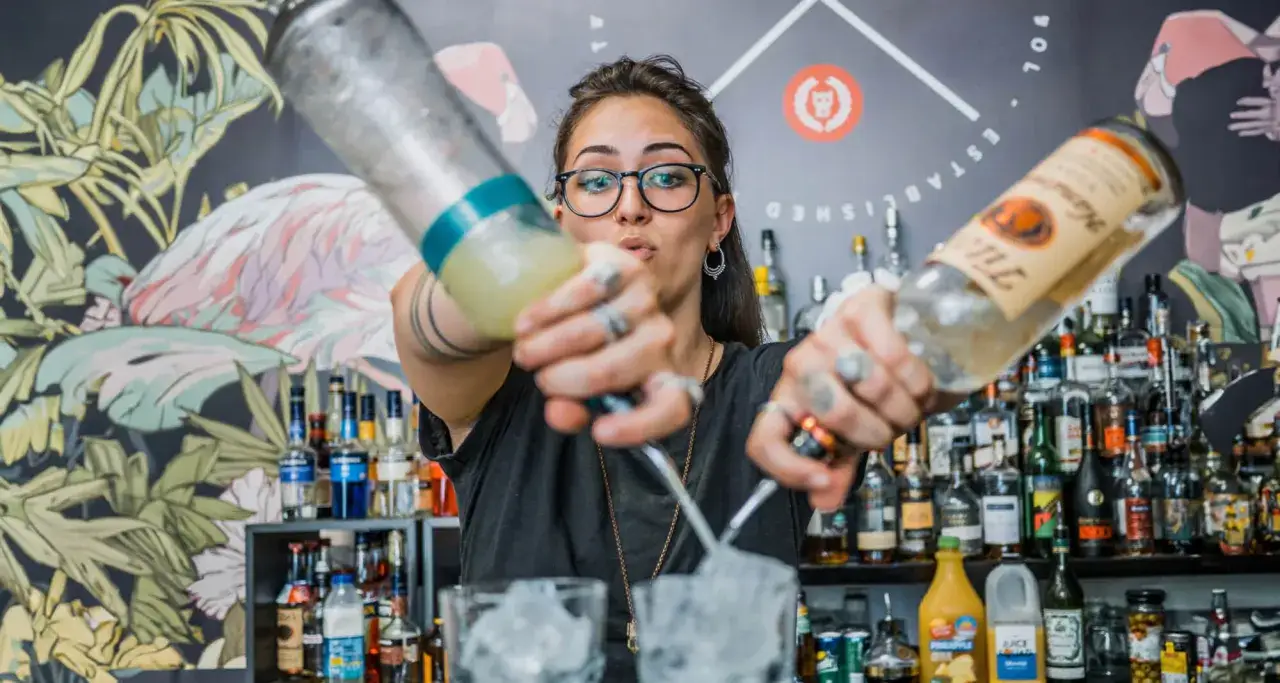 Zwinny barman przygotowuje drinki, nalewając płyny z dwóch butelek do szklanek z lodem.