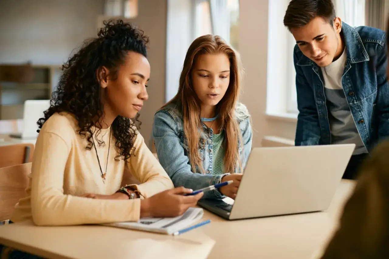 Uczniowie dyskutują nad projektem, analizując materiały na laptopie. Wybór kierunków technikum to ważny krok w ich edukacji.