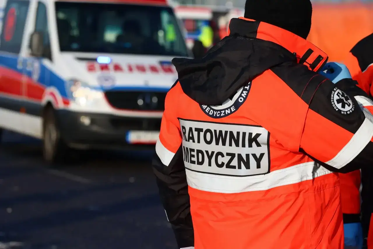 Ratownik medyczny w pomarańczowej kurtce stoi obok karetki. Zastanawiasz się, ile zarabia ratownik medyczny?
