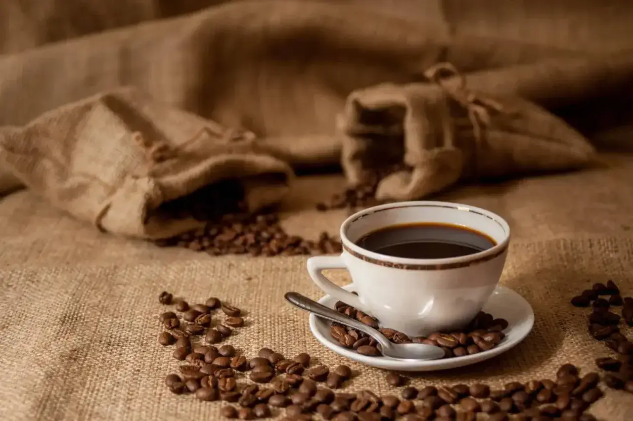 Aromaticzne ziarna kawy rozsypane wokół filiżanki czarnego napoju, jakby przygotowane przez doświadczonego baristę.