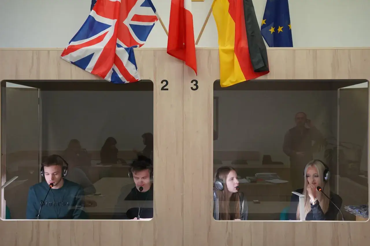 Studenci w słuchawkach ćwiczą lingwistykę stosowaną w kabinach tłumaczeniowych, z flagami Wielkiej Brytanii, Polski, Niemiec i UE.