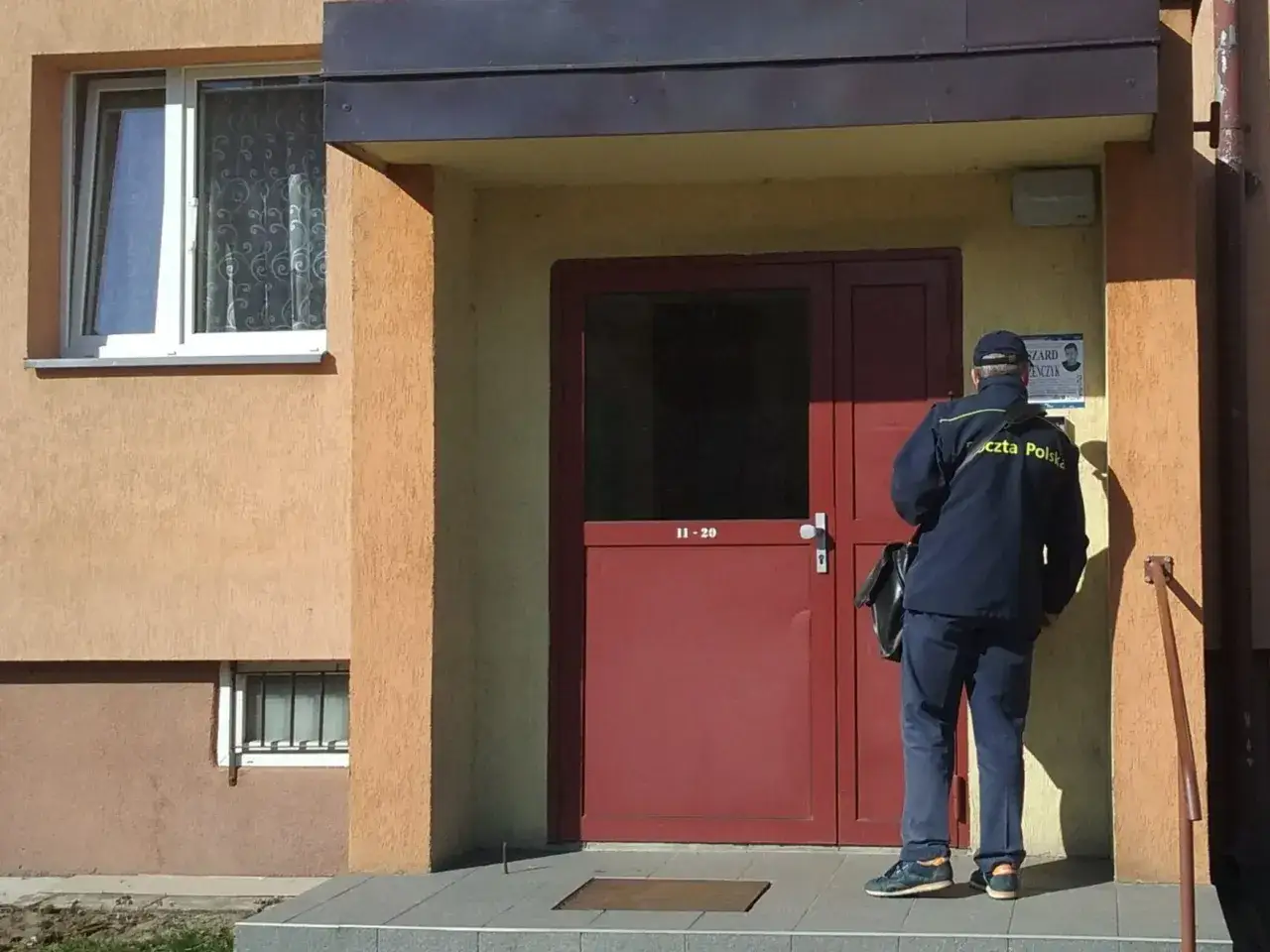 Listonosz w granatowym mundurze Poczty Polskiej stoi przed drzwiami. Zastanawiasz się, ile zarabia listonosz?