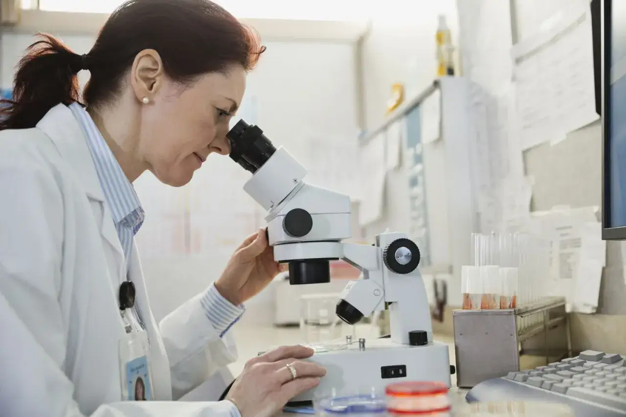 Patomorfolog w białym fartuchu bada próbkę pod mikroskopem w laboratorium.